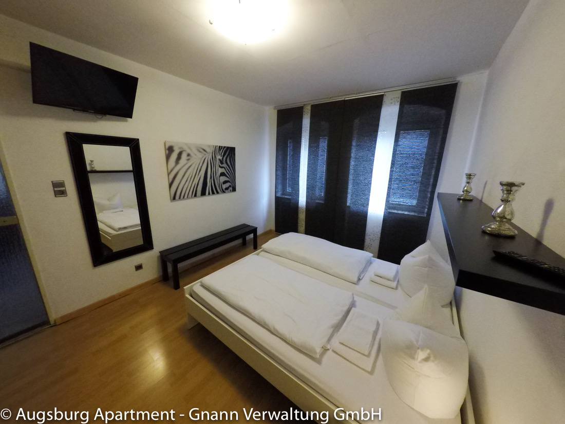 Schlafzimmer mit Doppelbett und TV in einem möblierten Apartment in Augsburg