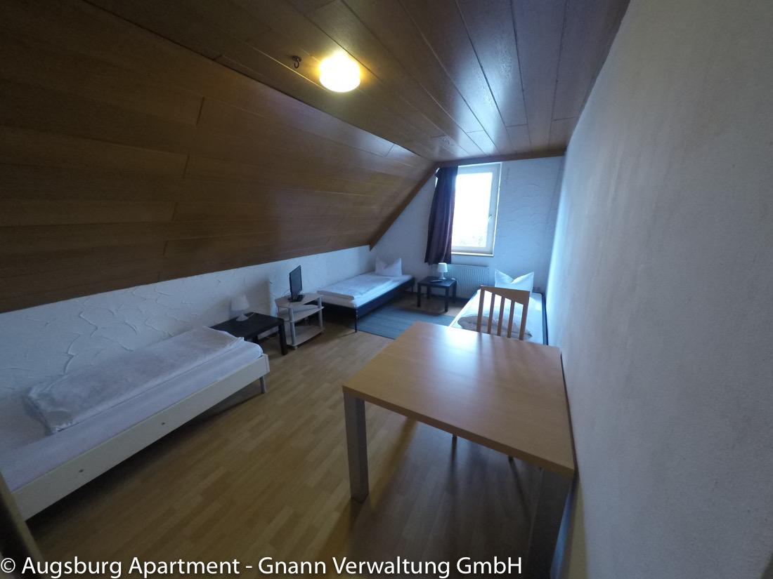 Room with two beds and a dining table in a workers' apartment in Augsburg