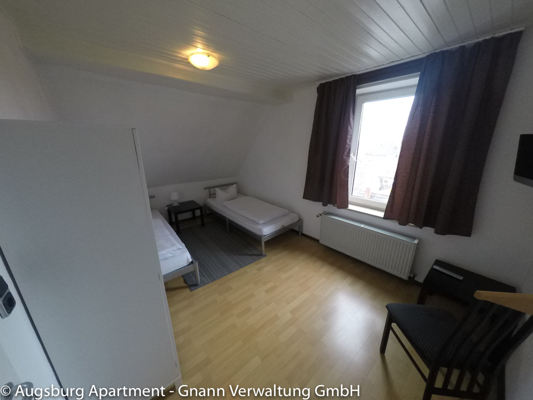 Twin room with single beds and a table in a workers' apartment in Augsburg