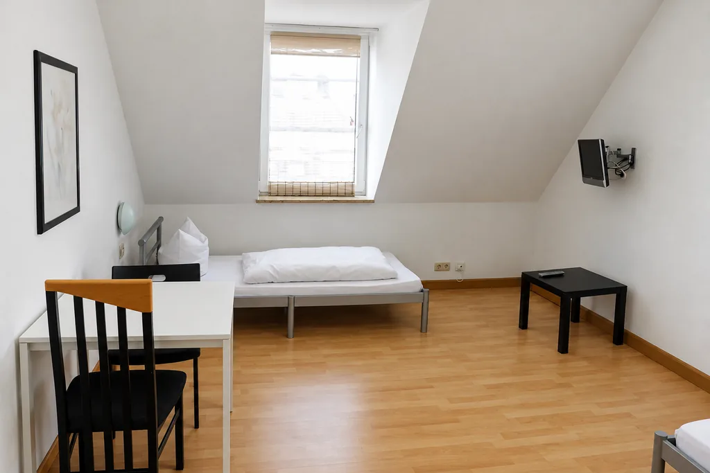 Helles Zimmer mit Dachschräge, Bett und Schreibtisch in einer Monteurwohnung