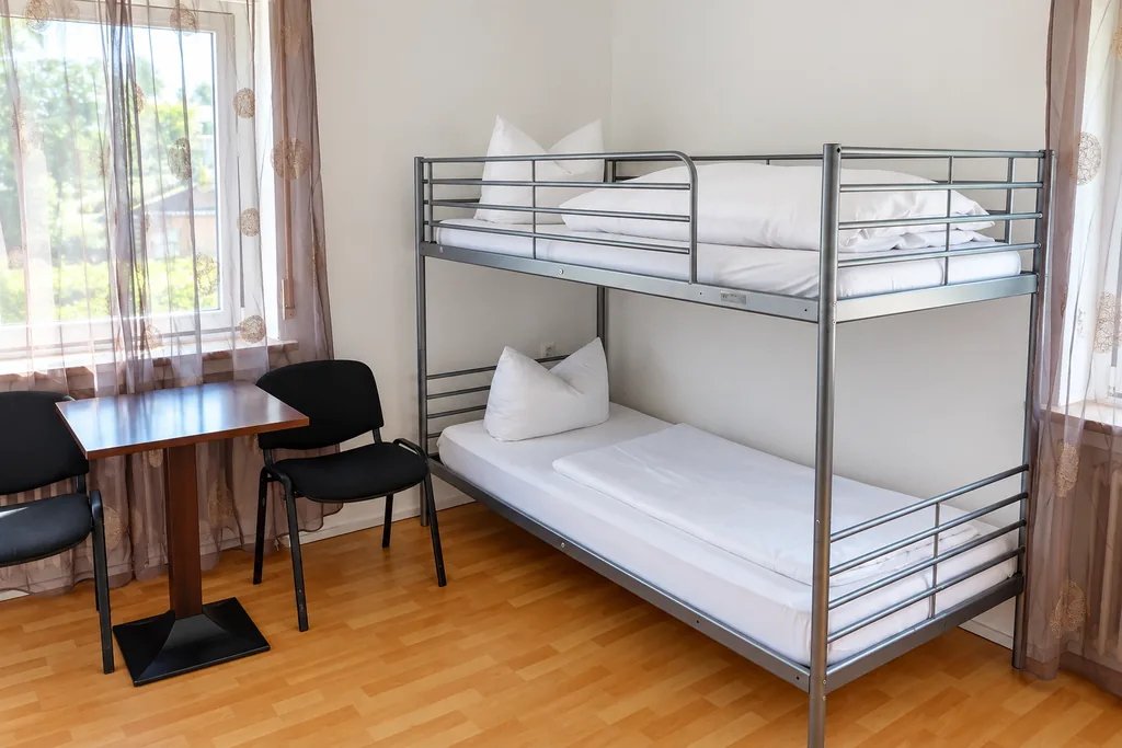 Monteurzimmer mit Etagenbett, Tisch und Stühlen am Fenster